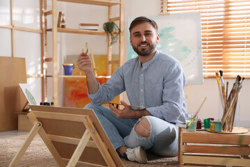 Sticker - Young man painting on easel with brush in artist studio