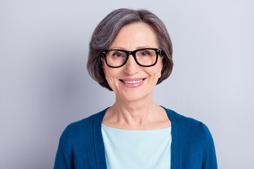 Poster - Photo portrait of happy elder woman with grey hair wearing glasses blue cardigan smiling isolated on grey color background