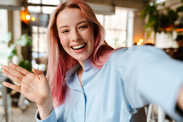 Wall Mural - Young woman with pink hair smiling and taking selfie photo in cafe