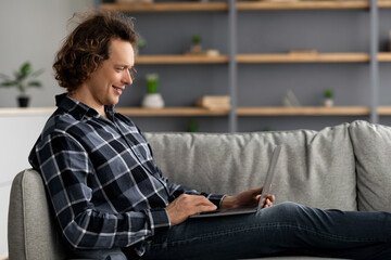 Poster - Freelancer Guy Using Laptop Sitting On Couch At Home, Side-View