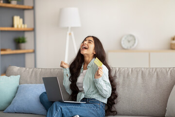 Wall Mural - Excited Indian lady with laptop and credit card gesturing YES, happy over enormous discount in online store at home