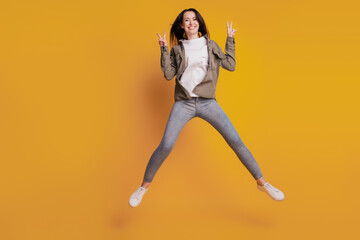 Full size photo of young careless woman jump show v-sign isolated on yellow background