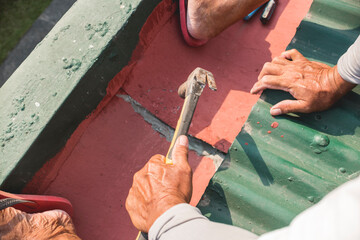 A man does DIY repair on the roof, hammering two sheets of a gutter together.