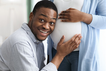 Wall Mural - Emotional black father leaning to pregnant wife belly