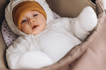 little cute baby girl dressed in winter clothes lying in a stroller on a walk