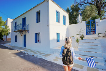 Wall Mural - Young traveling woman in hat with rucksack and national greek flag walking on old town enjoying the view.