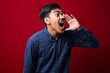 © Reza - Young asian man wearing casual shirt style shouting and screaming loud to side with hand on mouth