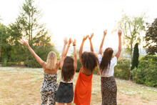Multi-ethnic Female Friends Standing With Hands Raised In Park