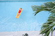 Enjoying suntan. Tropical vacation concept. Top view of young woman on the yellow air mattress in the swimming pool with palm trees.