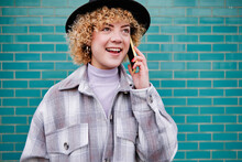 Smiling Woman Looking Away While Talking On Mobile Phone Against Blue Wall