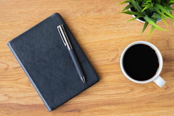 Wall Mural - Top view of black closed cover blank notebook with coffee cup and pen for taking write notes on wood table background. Flat lay, creative workspace office. Business-education concept with copy space.