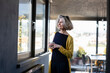 © Emma Innocenti/Westend61 - Smiling woman with coffee cup looking through window while standing at home