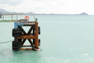 Old rusty mooring bollard with used truck tires on docks.