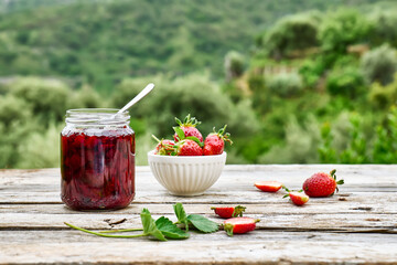 Wall Mural - Strawberry jam in a jar and fresh red ripe organic bio strawberries in a bowl on wooden table in the garden. Spring or summer harvesting. Healthy eating. Vitamin.