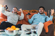 © Josu Acosta/Westend61 - Young competitive friends playing video game sitting on sofa in living room