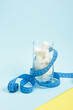 measuring tape and glass with sugar cubes on light blue and yellow background, overweight and malnutrition concept