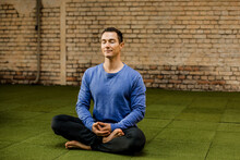 Male Athlete With Cross Legged Meditating Against Brick Wall In Health Club