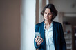 © Robijn Page/Westend61 - Businesswoman holding smart phone while leaning on wall at home office