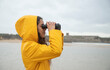 © Sebastian Kanzler/Westend61 - Young woman looking through binoculars while standing at beach