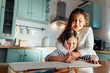 © Miguel Frias/Westend61 - Girl coloring on paper while sister hugging from behind in kitchen
