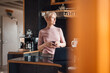 © Robijn Page/Westend61 - Smiling businesswoman looking away while holding coffee cup in kitchen at home office