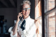 © Robijn Page/Westend61 - Smiling freelance worker looking through window while talking on mobile phone at home