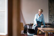 © Robijn Page/Westend61 - Smiling businesswoman with laptop sitting on desk while looking away at home office