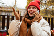 © alev/Westend61 - Smiling woman wearing knit hat gesturing while sitting at sidewalk cafe