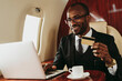 © OneInchPunch/Westend61 - Smiling businessman with credit doing online shopping through laptop in airplane