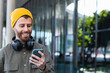 © NOVELLIMAGE/Westend61 - Smiling handsome man with headphones using smart phone near building