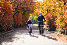 Cheerful Mother And Daughter Cycling In Park During Autumn
