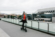 © Xavier Lorenzo/Westend61 - Happy woman riding electric push scooter on footpath near railing in city
