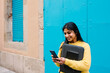 © Xavier Lorenzo/Westend61 - Smiling woman with digital tablet and laptop bag using mobile phone against blue wall