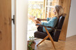 © steve brookland/Westend61 - Woman with digital tablet sitting on armchair at home