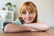 © steve brookland/Westend61 - Smiling girl with arms crossed sitting at table in living room