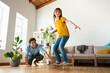 © steve brookland/Westend61 - Father helping daughter to ride skateboard in living room at home