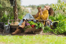 Laughing Woman Holding Fresh Broccoli While Sitting On Bench In Garden