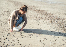 Young Woman Drawing Heart On Sand At Beach