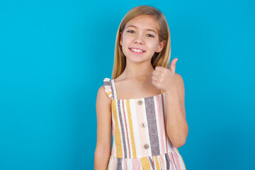 beautiful Caucasian little girl wearing stripped dress over blue background giving thumb up gesture, good Job! Positive human emotion facial expression body language.