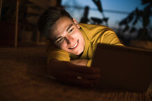 Smiling Man Using Tablet While Lying On Carpet In Living Room During Night