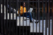 © Veam/Westend61 - Disabled man with leg prosthesis using laptop while sitting on steps seen through metal railing