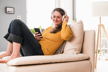 Relaxed Woman Enjoying Music While Sitting On Sofa In Living Room