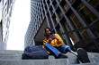 © Veam/Westend61 - Young man with artificial limb using mobile phone while sitting on steps against skyscraper