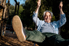 Happy Senior Man Playing While Sitting On Swing At Park