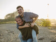 © Gustafsson/Westend61 - Cheerful father carrying son piggyback at riverbank