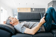 © Josep Rovirosa/Westend61 - Smiling mature man with digital tablet day dreaming while lying down on sofa in living room