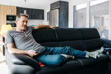 Mature Man Holding Remote Control While Sitting On Sofa At Home