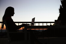 Silhouette Of Woman Working On Laptop On Balcony During Sunrise