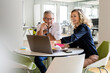 © peter scholl/Westend61 - Smiling businesswoman pointing at laptop while sitting by mature businessman at table during meeting in office