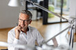 © peter scholl/Westend61 - Smiling businessman with hand on chin looking away while sitting in office